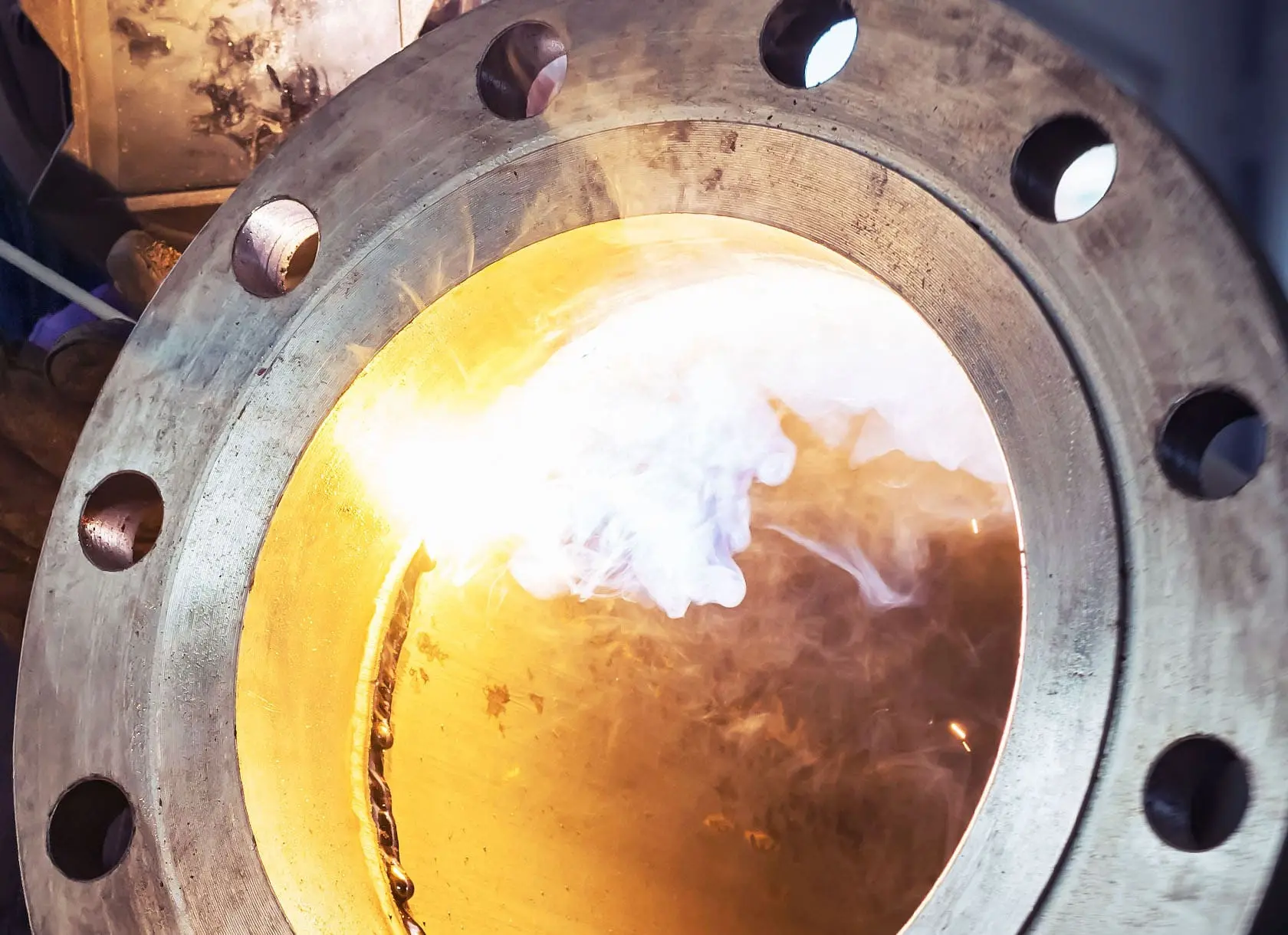A flange being welded, with smoke rising from the weld inside the bore