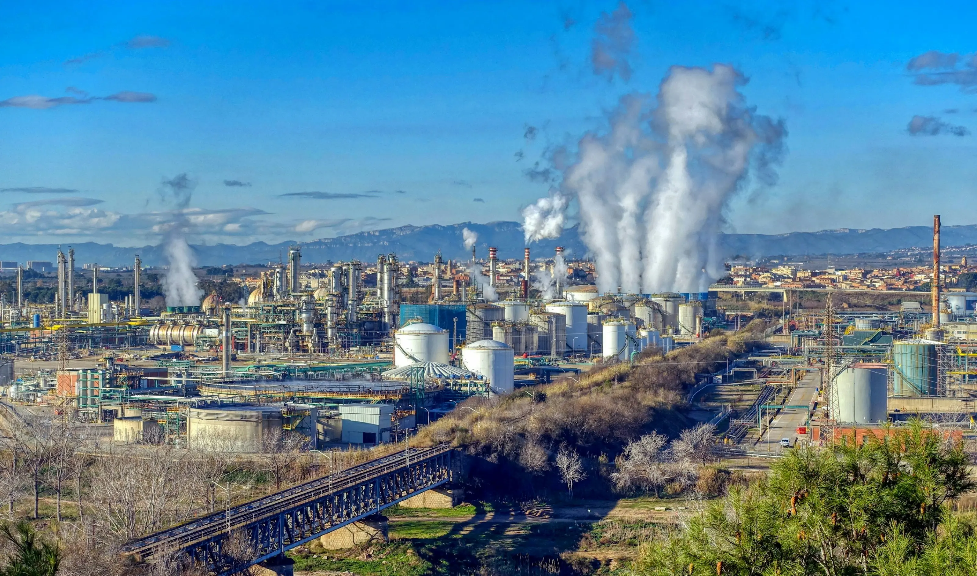 A chemical plant with white storage tanks and steam rising from its stacks
