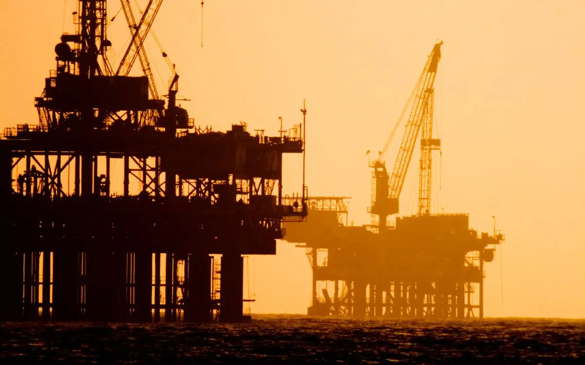 Offshore oil platforms silhouetted against an orange evening sky