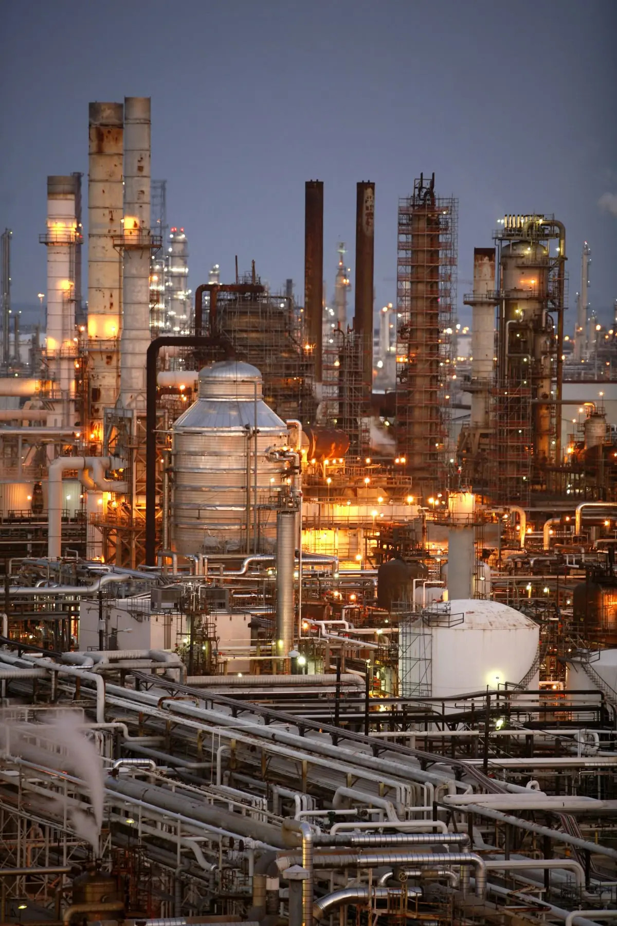 A petrochemical plant at dusk, with lit columns, stacks and pipe racks